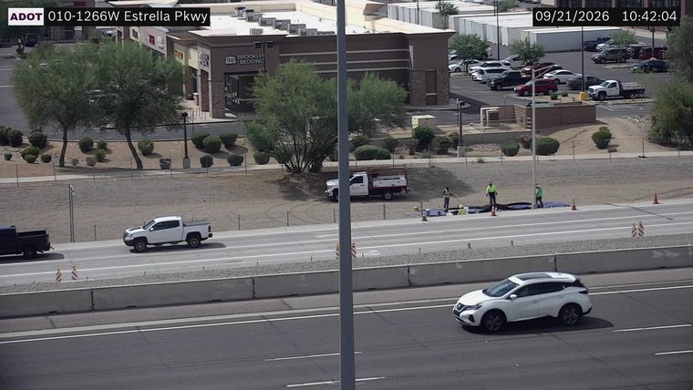 Three workers and a utility truck on the right shoulder with cones