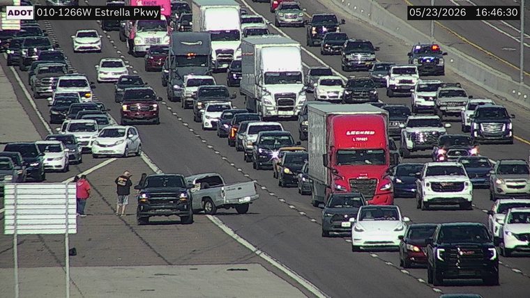 Two pickup trucks involved in a collision on the left shoulder/gore area with two people standing outside