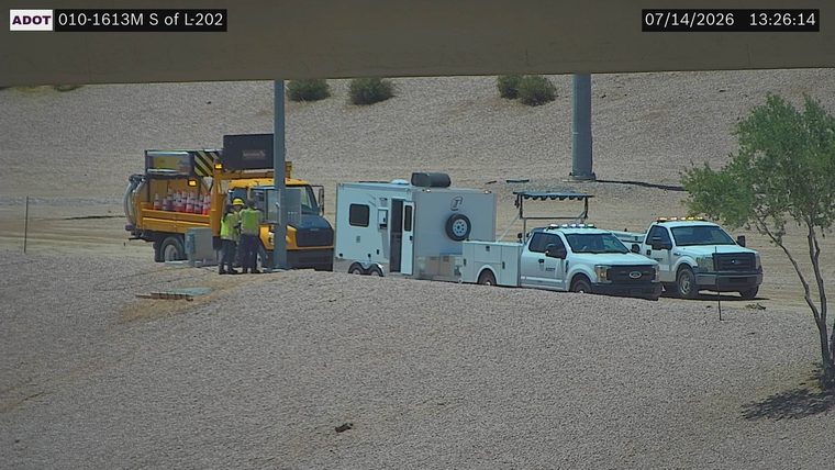 Two workers in high-visibility vests near a yellow truck with cones, and two white trucks with amber lights