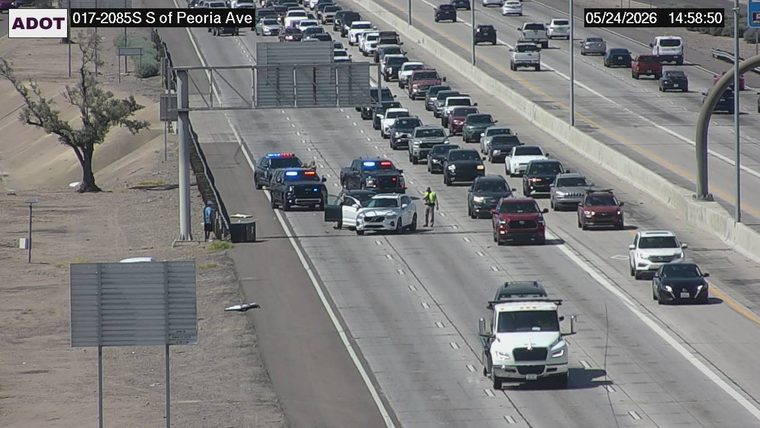 Multiple police vehicles with flashing lights and an officer standing next to a white SUV with an open door in the left lanes