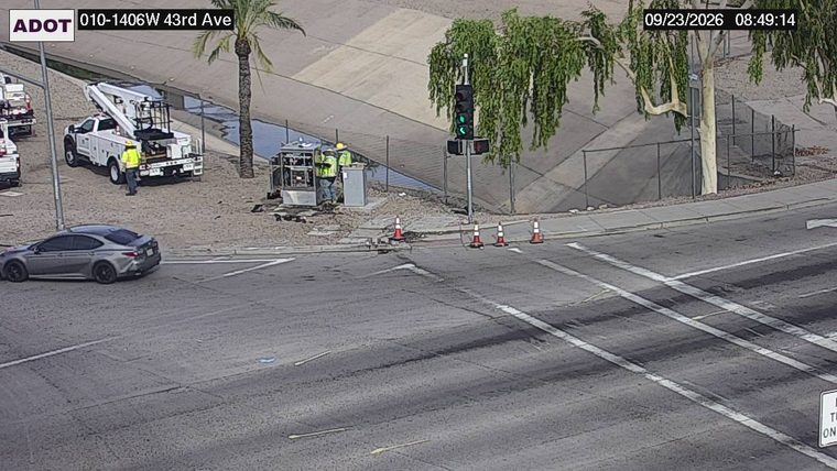 Two workers in high-visibility vests near traffic signal equipment with traffic cones on the roadway