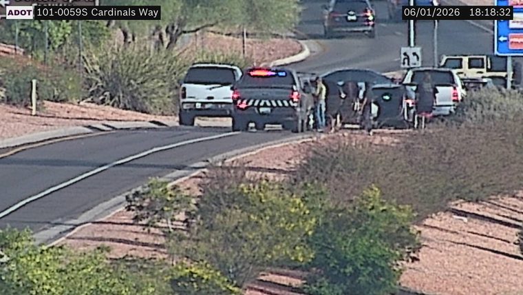Police vehicle with lights on and two people standing near a vehicle on the right shoulder