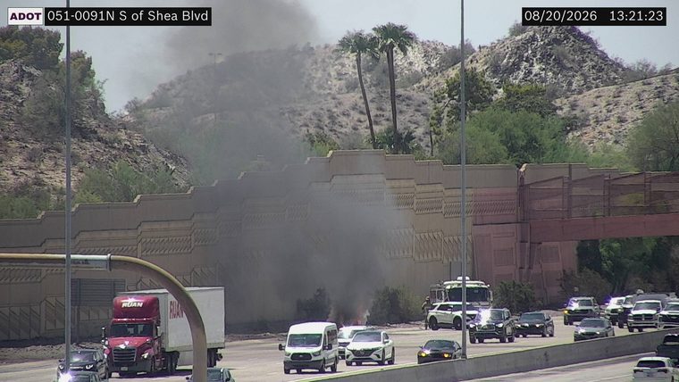 Smoke and flames visible in the median, with a fire truck and personnel present