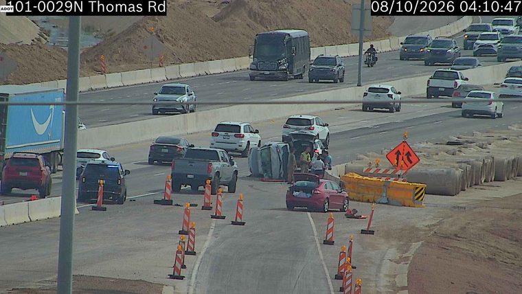 A vehicle is overturned in the roadway with several people around it.