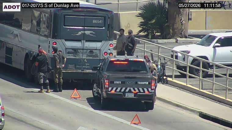 State Trooper vehicle with emergency lights on and warning triangles on the roadway behind a bus, with several people standing nearby