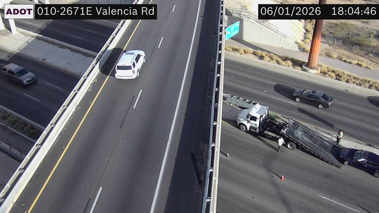 Tow truck with a car on its flatbed and two people standing nearby on the right shoulder