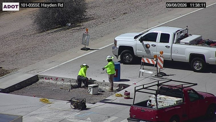 Two workers in high-visibility vests and hard hats are present near construction equipment and materials.