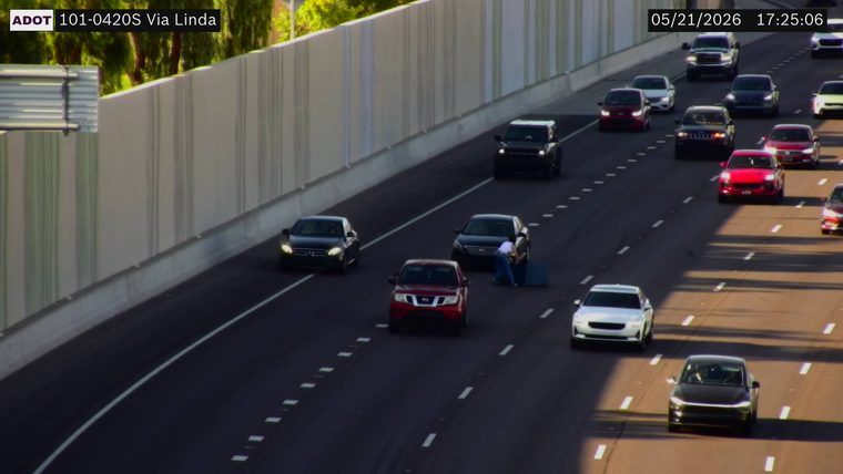 Person standing in the travel lane behind a black sedan next to a blue object