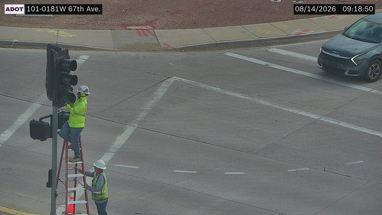 Two workers on a ladder repairing a traffic signal