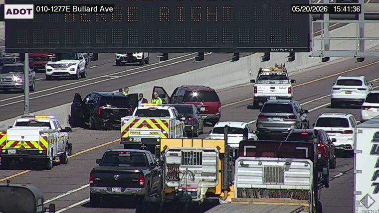 A multi-vehicle crash on the left shoulder and left lane with ADOT Service Patrol trucks present and people standing outside a damaged black SUV with open doors