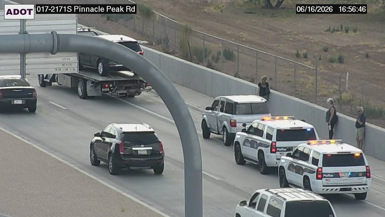 Two police cars with lights on and three people standing near the barrier