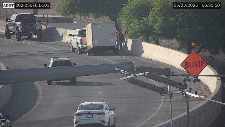 White pickup truck towing a trailer on the right shoulder and a black pickup truck on the left shoulder, both with people standing outside