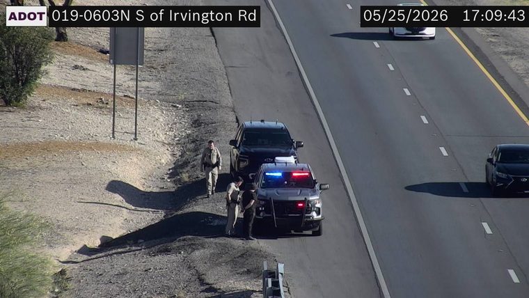 Police vehicle with flashing lights and officers on the left shoulder