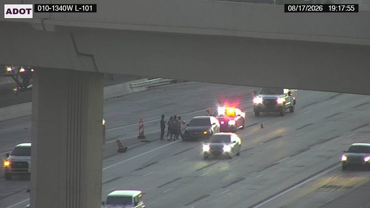 Police car with red and blue lights on the roadway, surrounded by several people