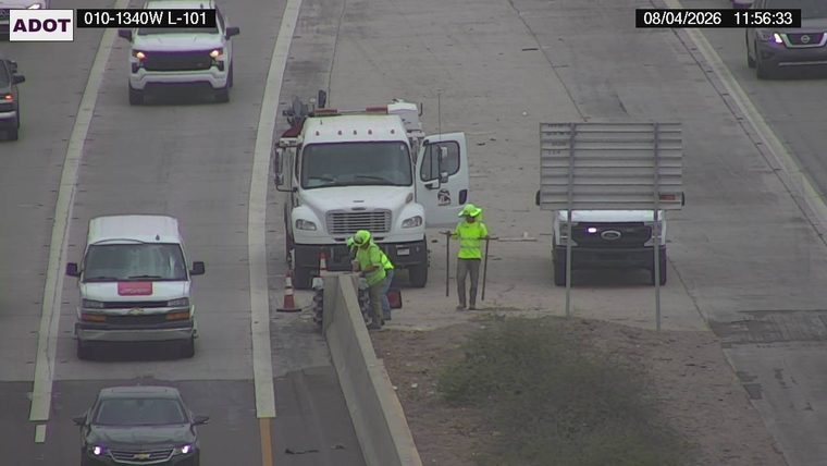 Two workers in high-visibility vests and hard hats near a white truck on the right shoulder