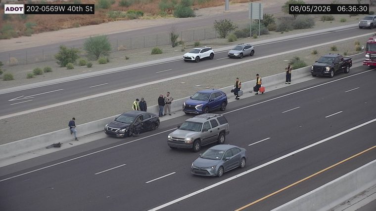 Black sedan with visible collision damage in the left lane, with two individuals in high-visibility vests and two law enforcement officers standing nearby