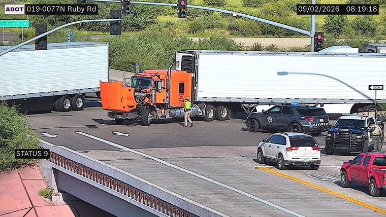 Two police vehicles and a person in a high-visibility vest near an orange semi-truck with its hood up
