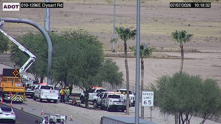 Several vehicles and workers on the shoulder near a construction crane
