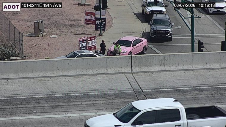 Two people standing next to a pink car on the right shoulder