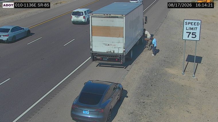Two people by a box truck on the right shoulder