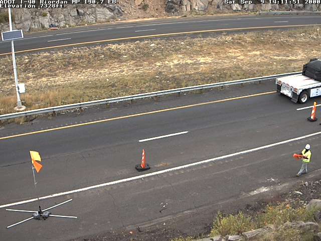 Worker with safety vest and hard hat holding traffic control device in the right lane