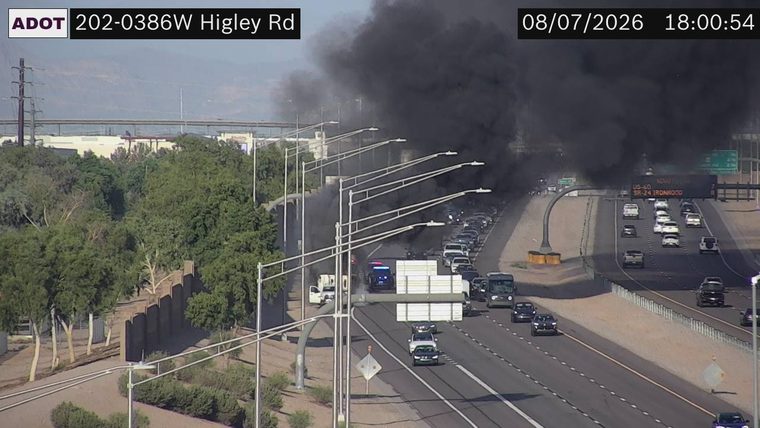 Thick black smoke and flames visible in the right lanes, with a police car present