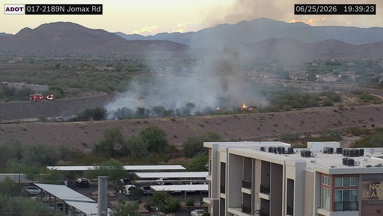 Fire and smoke in the vegetation off the right side of the roadway, with two fire trucks present on the embankment above.