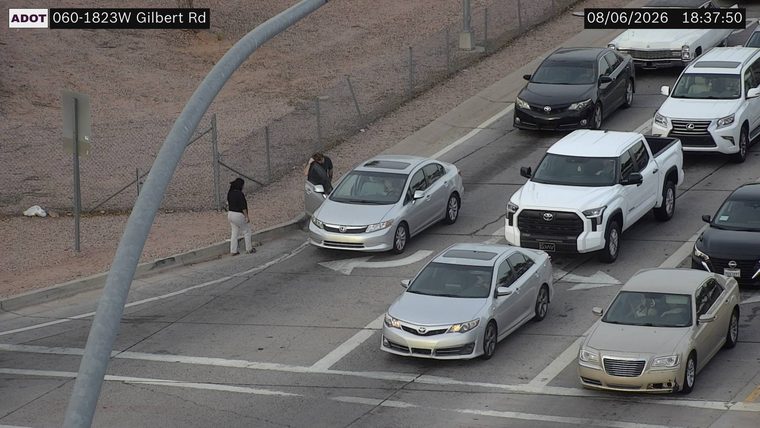 Two people standing next to a silver sedan on the left side of the roadway