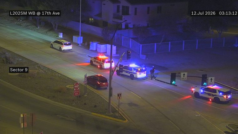 Two police cars with red and blue lights on, and two officers visible, near a red car.