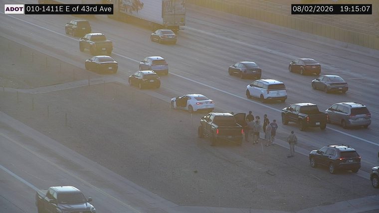 Several people gathered near a white car with its door open and a black pickup truck on the shoulder