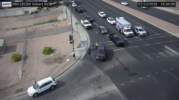 Police SUV with red and blue lights on, two officers present, and traffic cones in the intersection