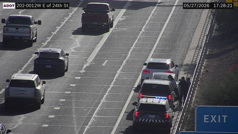Police vehicle with emergency lights on the right shoulder behind stopped vehicles and people standing outside