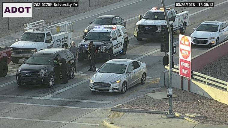 Police vehicle with flashing lights and officers standing on the roadway next to a stopped black SUV