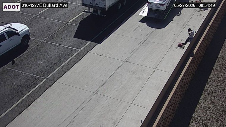 Person sitting on the concrete barrier on the right shoulder next to a small cart