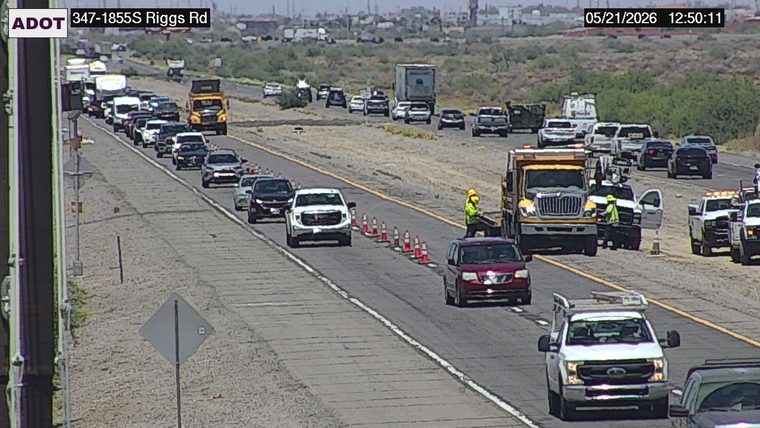 Construction workers in high-visibility vests and traffic cones on the right side of the roadway near work vehicles