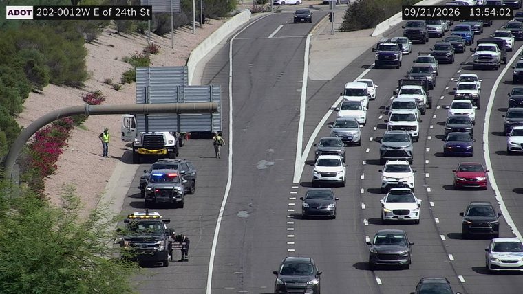 Police car with red and blue lights on the shoulder next to a large truck and several workers