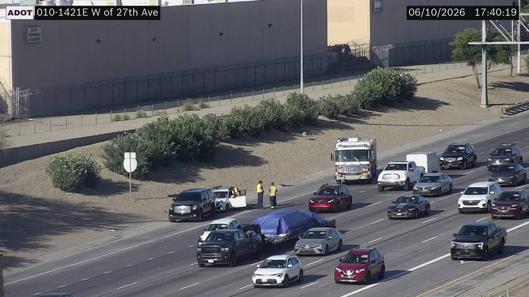 Two workers in high-visibility vests near a trailer covered with a blue tarp in the right lane