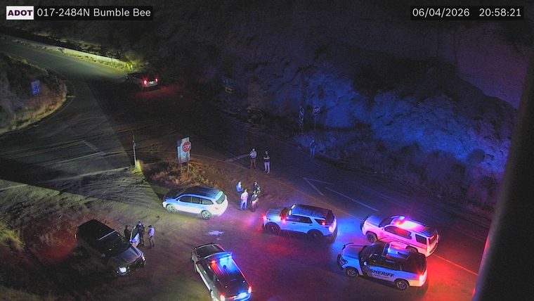 Multiple law enforcement vehicles and several individuals gathered on the roadway