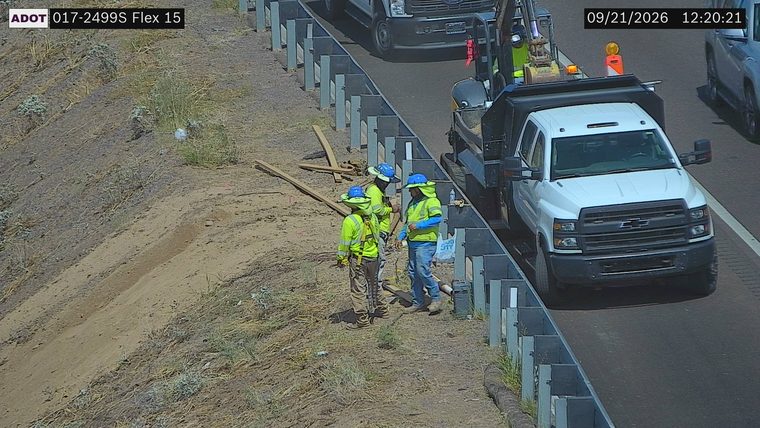 Three workers in high-visibility vests and hard hats on the shoulder near construction equipment and materials