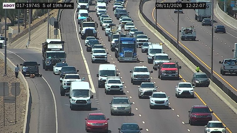 Two people attending to a flat tire on a dark pickup truck on the right shoulder