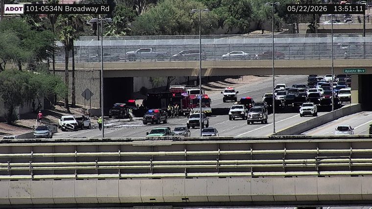 Multiple emergency responder vehicles with flashing lights and a crashed white vehicle on the left shoulder under the overpass