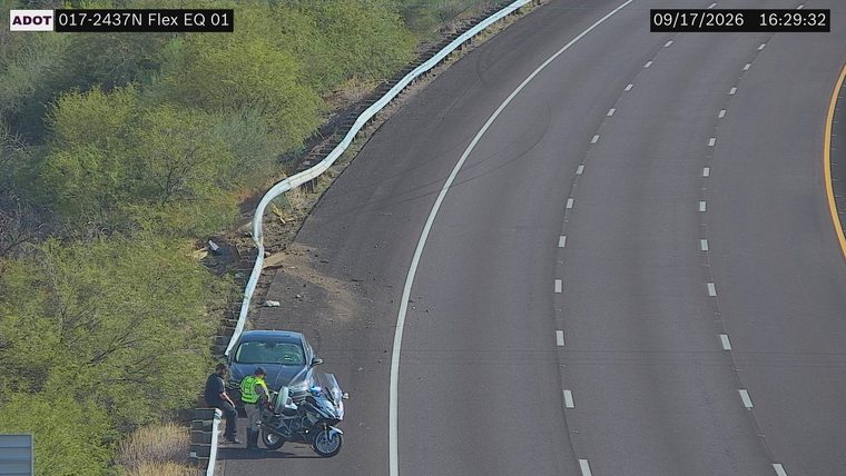 Police motorcycle with lights on next to a car on the right shoulder