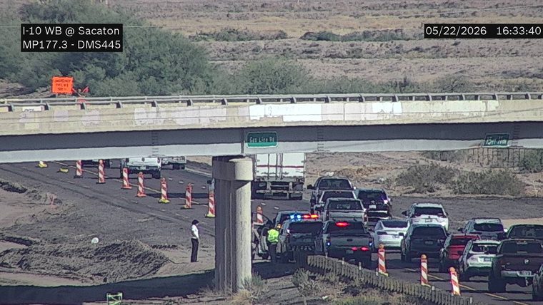 Police vehicle with flashing lights and responders standing on the shoulder under the overpass