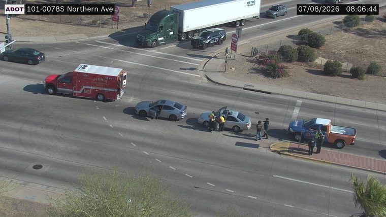 Ambulance and police car at intersection with people around two vehicles