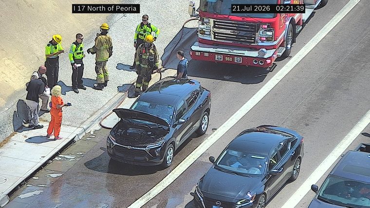 Fire truck and firefighters attending to a black SUV with its hood open on the right shoulder