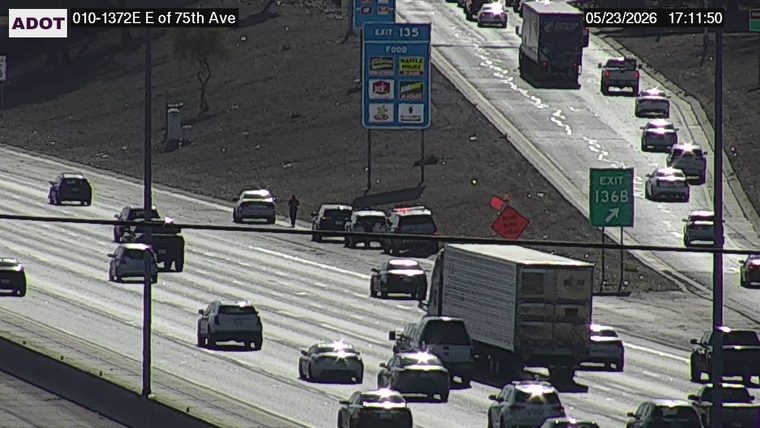 Pedestrian walking on the left shoulder next to a white vehicle