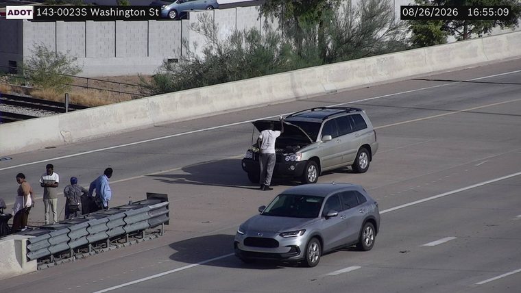 Silver SUV with hood open and a person attending to it in the right lane