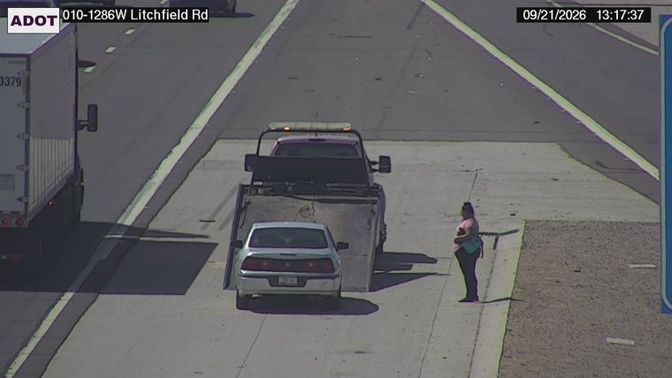 Tow truck with a car on its flatbed and a person standing nearby on the shoulder