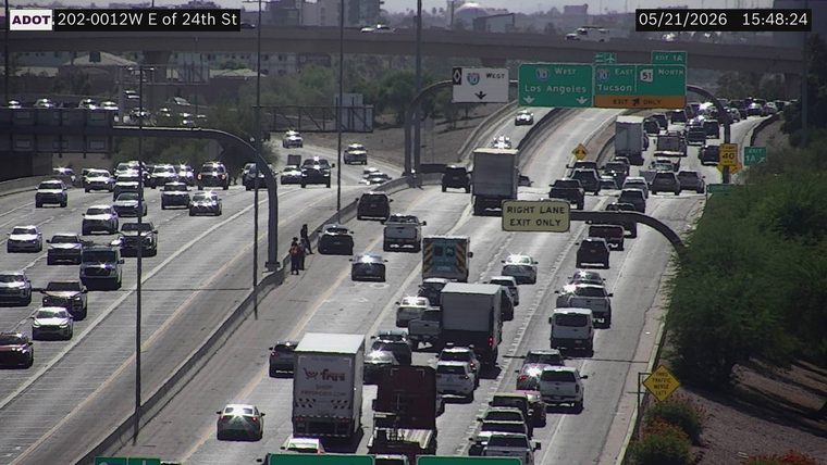 People standing outside a stopped black sedan on the left shoulder next to the median barrier