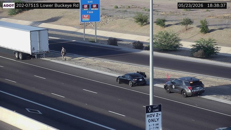 Police vehicle with lights on and an officer walking on the right shoulder next to a black coupe